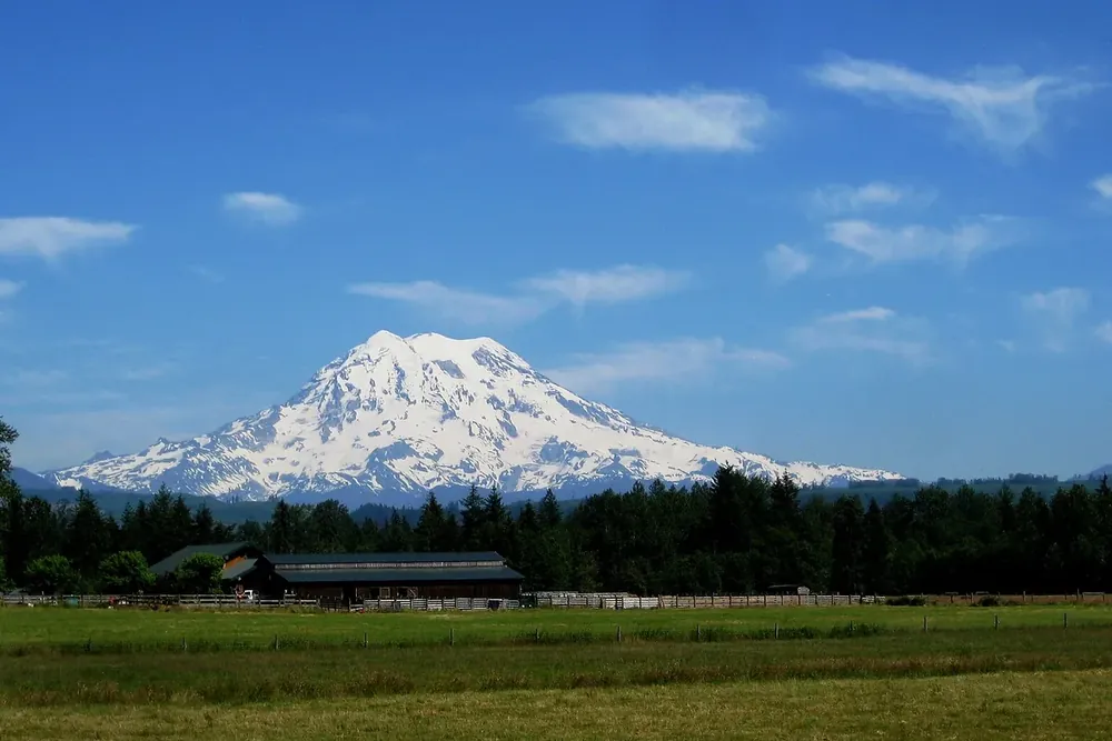 Mount Rainier above green farmland and farm buildings near Graham, Washington